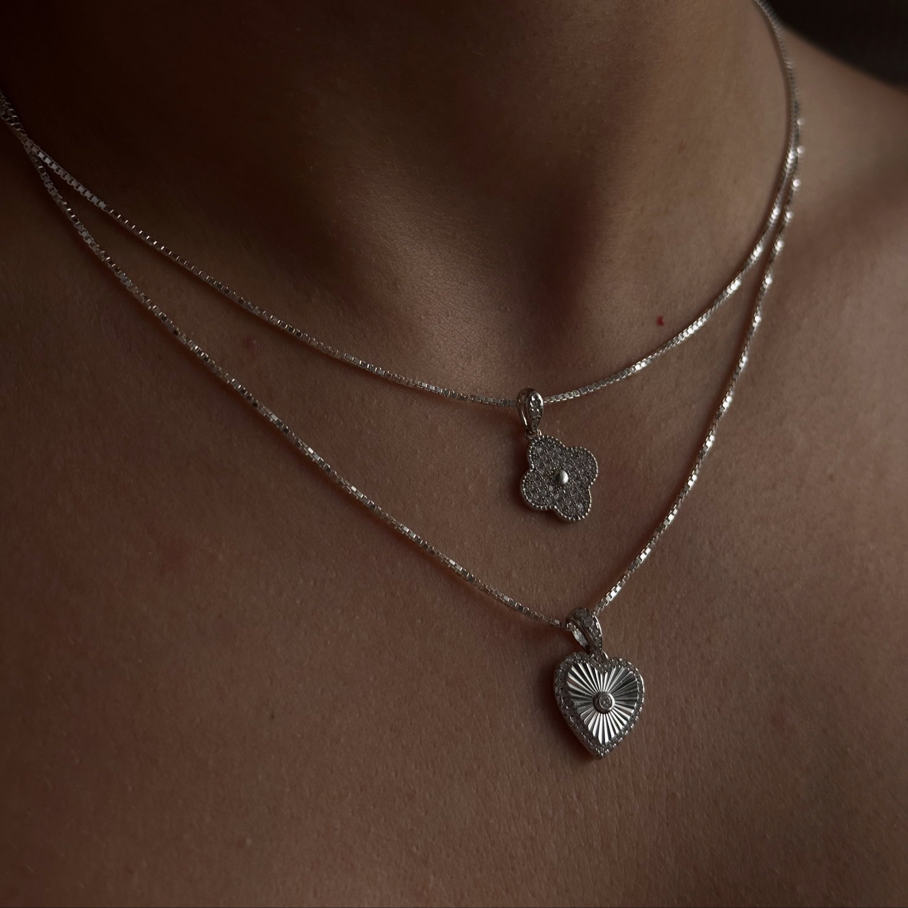Close-up of a person wearing two silver necklaces with heart-shaped pendants.