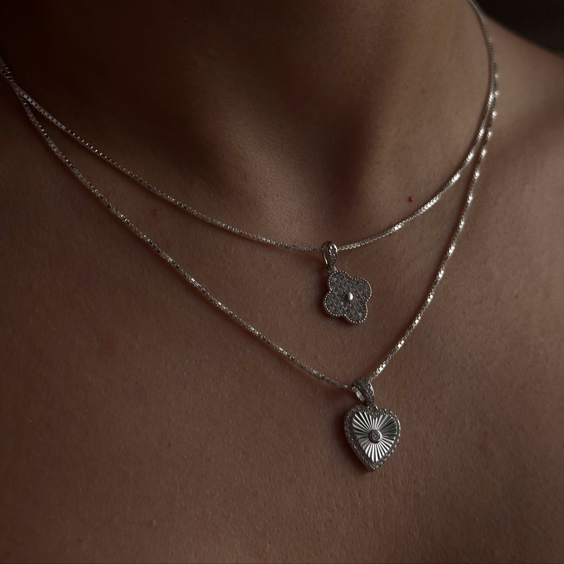 Close-up of a person wearing two silver necklaces with heart-shaped pendants.