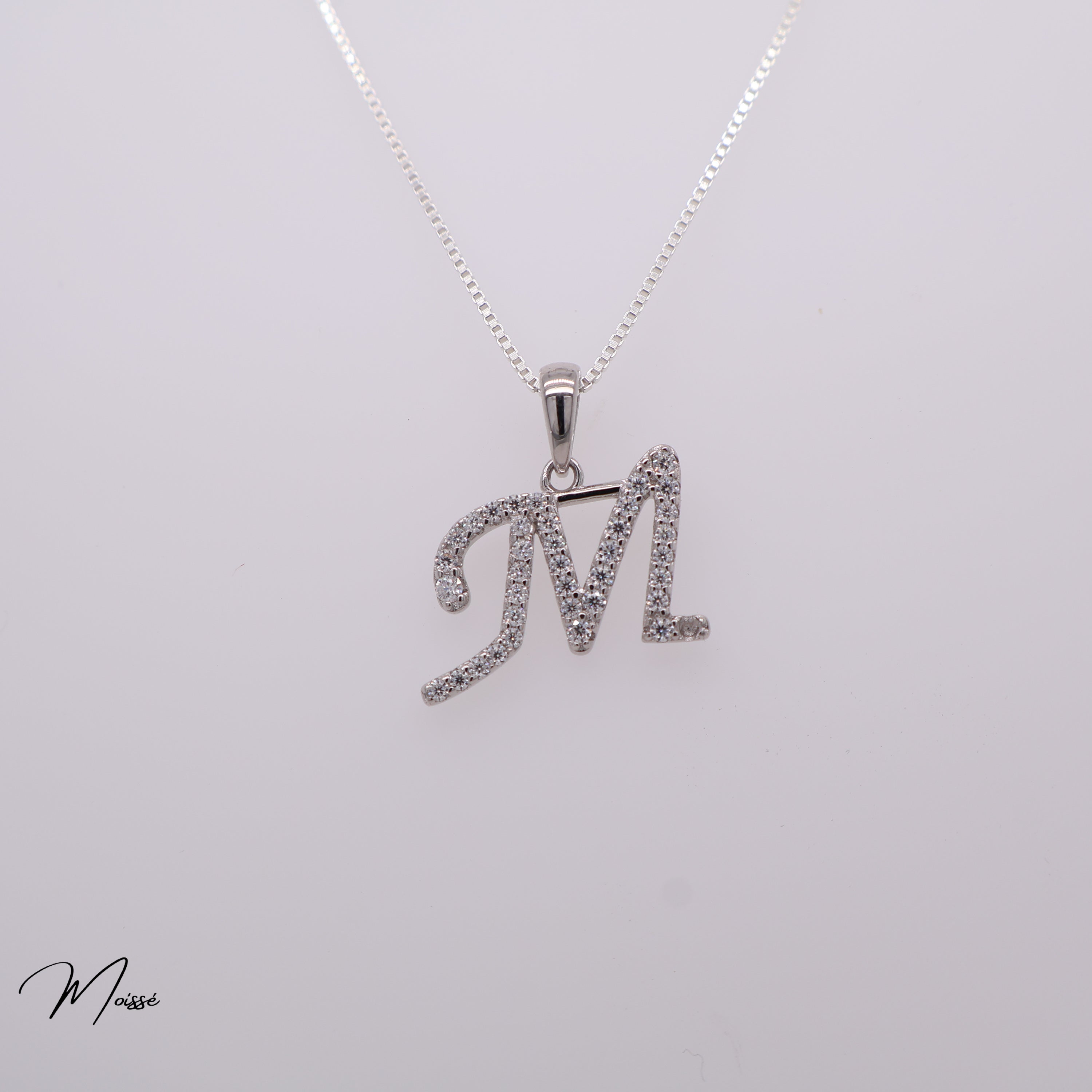 Silver necklace with 'M' pendant on a light gray background