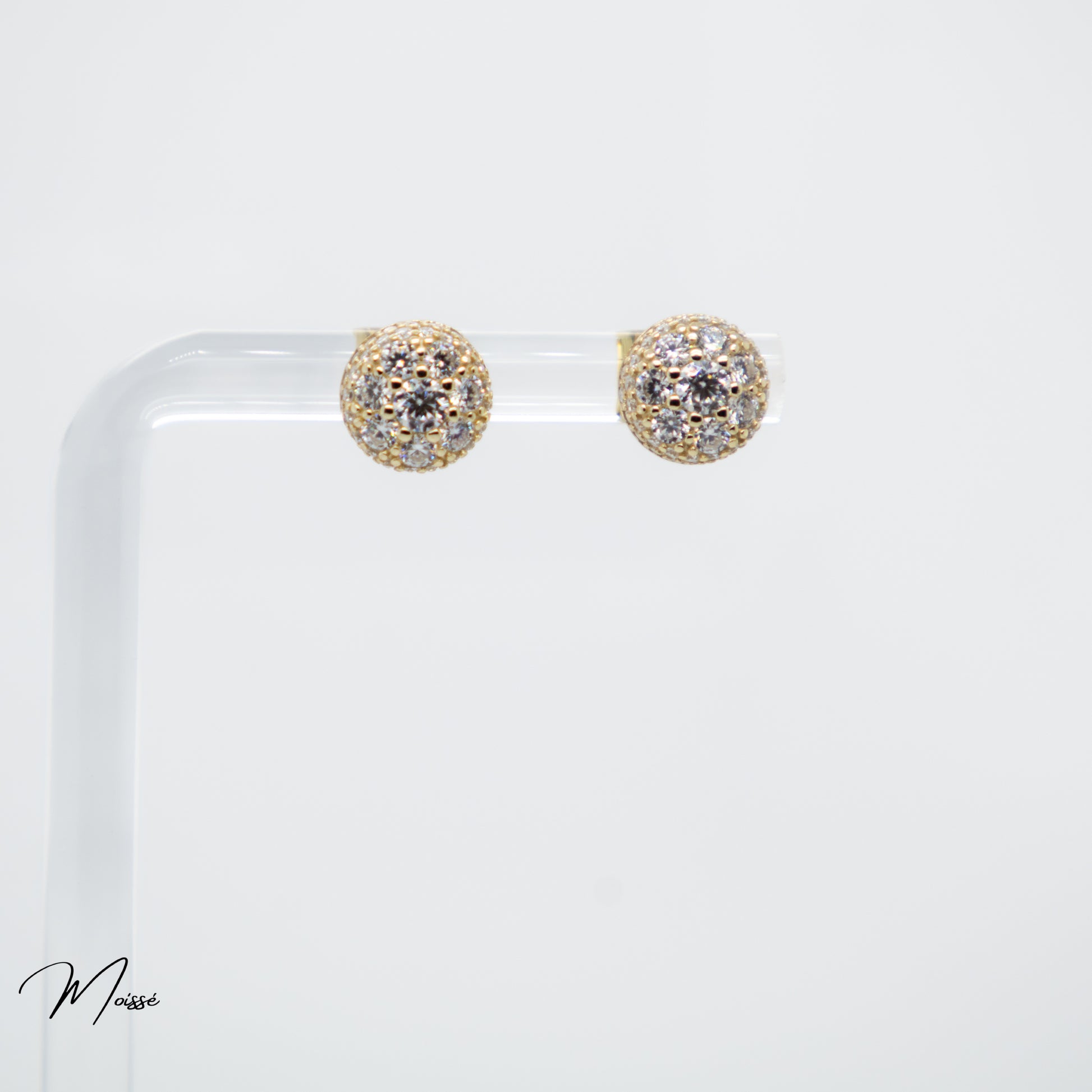 Gold and diamond earrings on a clear stand with a white background