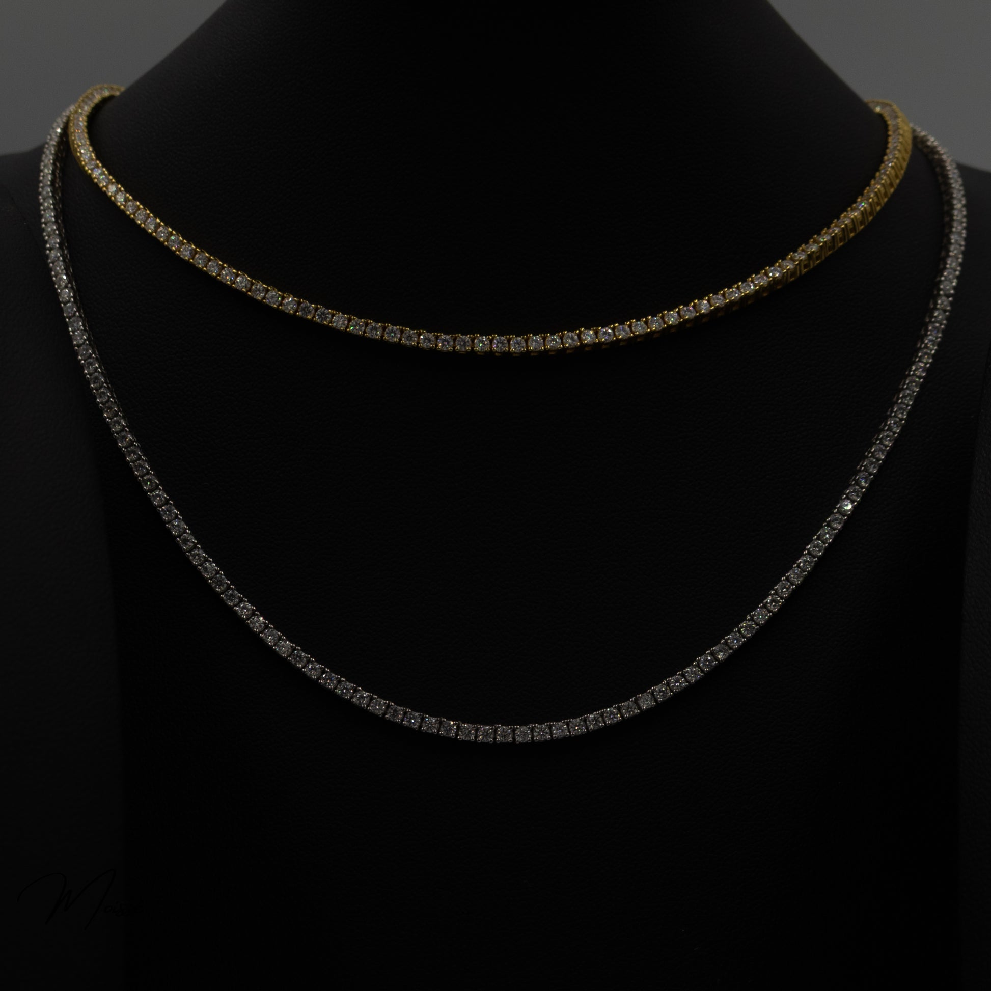 A gold vermeil and a sterling silver tennis necklace on a black display